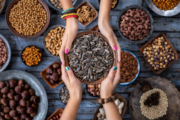 una ciotola di semi di girasole per mano di due donne e noci assortite sullo sfondo. - pistachio nut food snack foto e immagini stock