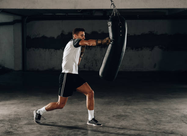 istock Aggressive boxer in boxing gloves training with punching bag 1361049532