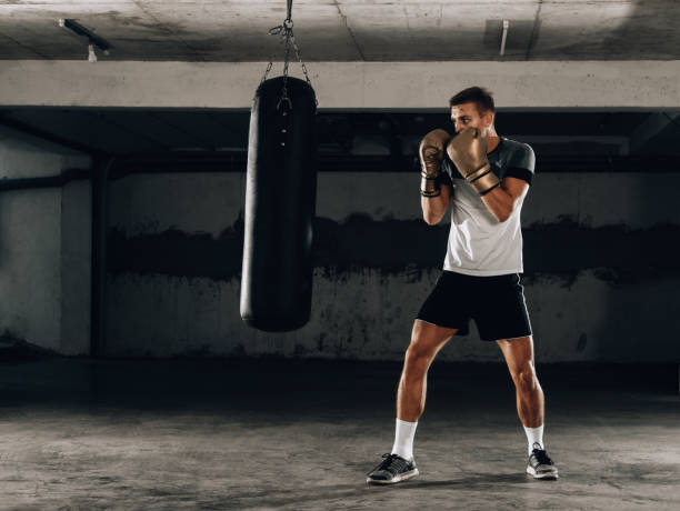 istock Male boxer in boxing gloves training with punching bag 1361049539
