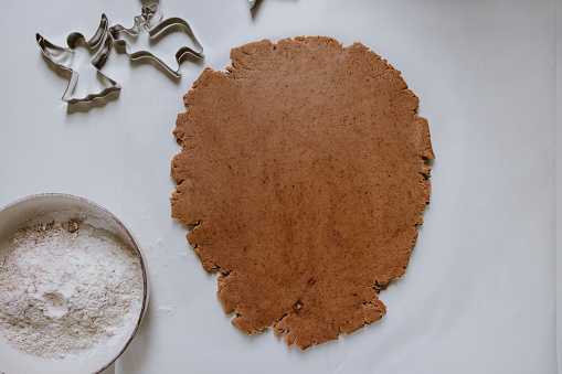 Top view of gingerbread pastry dough on a paper with cookie cutters and bowl with flour on the table with copy space.