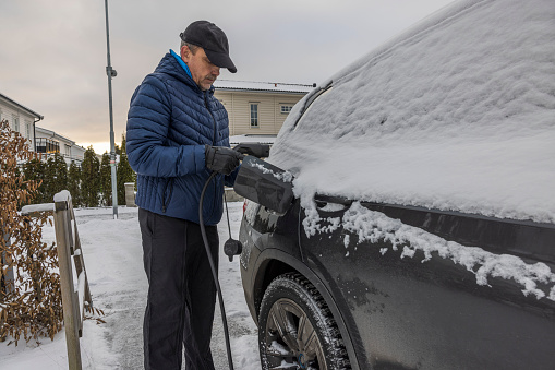 View of a man connecting a charging cable to an electric car charging station on a frosty winter day. Sweden.