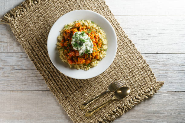 Vegan goulash on rice in bowl with dill, fork and spoon on rustic fabric