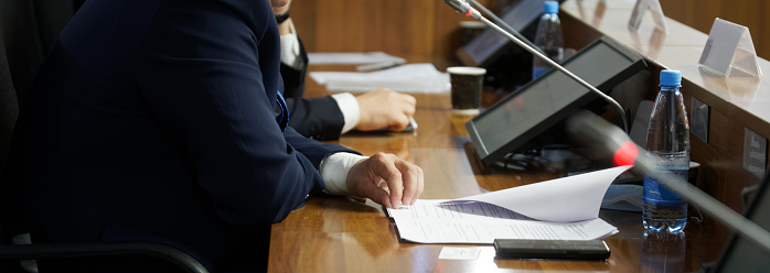 The hand of a man in a suit sitting at a table with monitors and speakerphones. The concept of negotiations, discussion, meeting or conference. Without a face