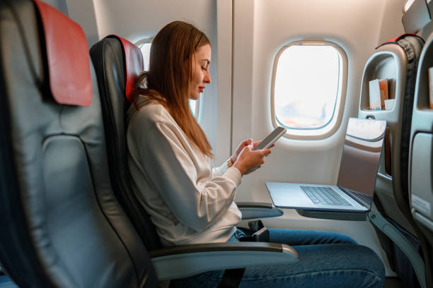 istock Young woman using laptop and cellphone in airplane 1361095726