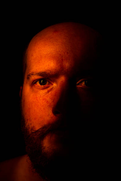 istock The bald man is looking at the camera and half his face is exposed. Red light hits it 1361098371