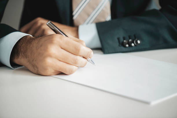 Man sits at a desk and fills in a pile of documents with a pen