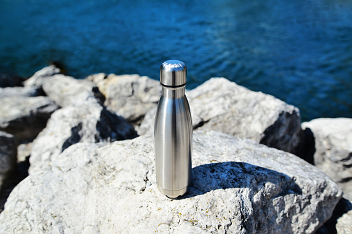 Close-up of steel eco thermo water bottle on the background of the lake in the mountains. Copy space. Zero waste, no plastic, sustainability. Reusable eco friendly sustainable water bottle.