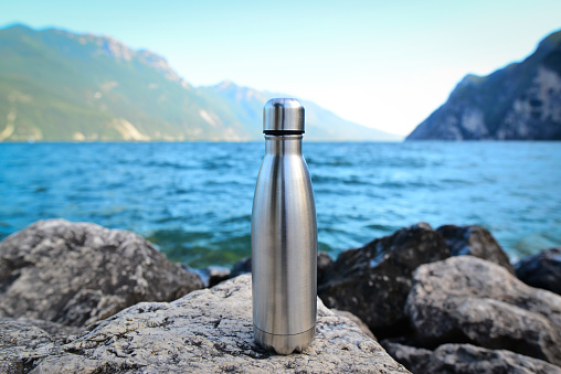 Steel eco thermo water bottle on the background of the lake in the mountains. Be plastic free. Zero waste. Copy space. Zero waste, no plastic.