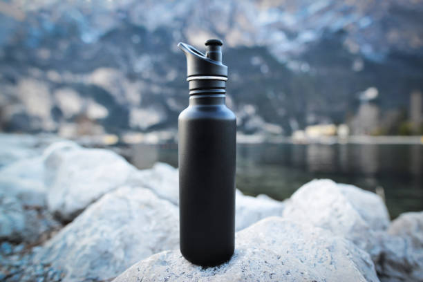 Close-up black of steel eco thermo water bottle on the background of the lake in the mountains. Copy space. Zero waste, no plastic, sustainability. Zero waste, no plastic, sustainability. blue reusable water bottle stock pictures, royalty-free photos & images