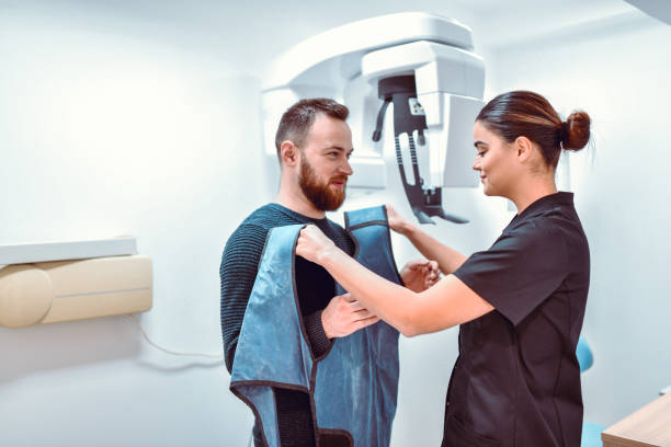 female dental radiologist preparing male patient for dental computer tomography - röntgen cihazı stok fotoğraflar ve resimler