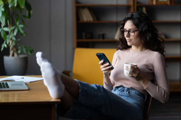 istock Woman remote employee procrastinate on workplace read text in cellphone distracted from laptop work 1361121347