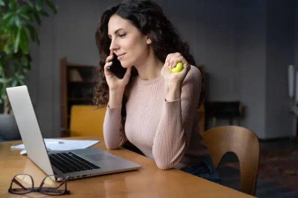 Photo of Multitasking businesswoman hold rubber expander tool in hand talking on mobile phone at workplace