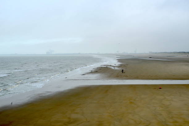 Blankenberge, West-Flanders, Belgium - December 24, 2021:  silhouette of a person searching precious metals with a metal detector, hoping to find some valuable objects left by tourists on the beach