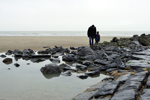 Blankenberge, West-Flanders, Belgium - December 24, 2021: Italian tourists, father and son paying attention not to fall when they walk on the breakwater rocks