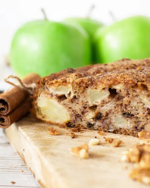 Soft apple cinnamon cake with walnuts on wooden table with crumbs and green Granny Smith apples in the background. Healthy vegan homemade dessert.