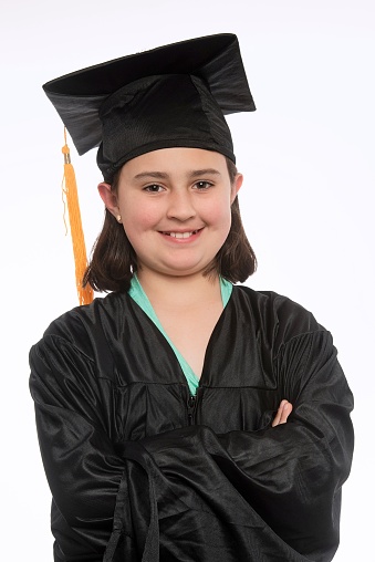 Spanish little girl looking at the camera wearing a graduation gown on white background