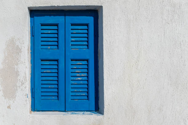Typical blue greek shutters closed on a window of a white wall house. Taken on a very sunny summer day in the Aegean Island of Santorini, Greece