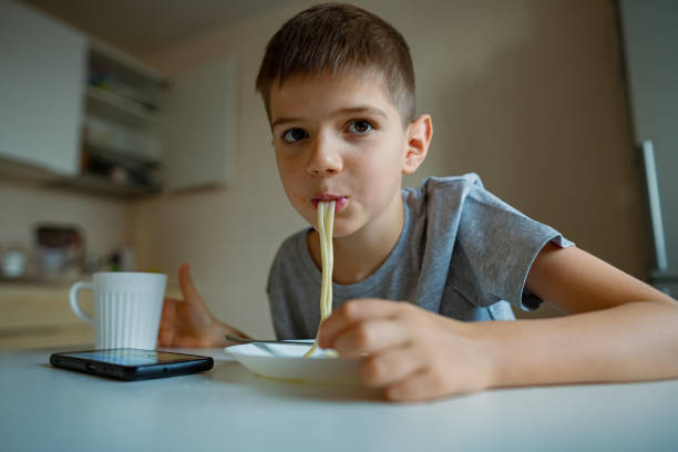 istock Cheerful, hungry boy eats pasta with appetite, sucks in pasta playfully 1361198427