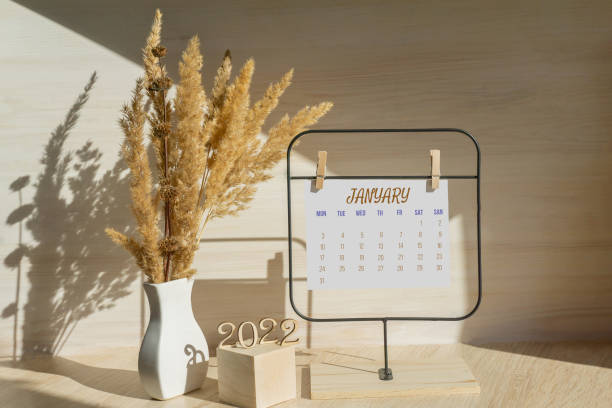 january 2022, calendar date. page from calendar on white paper on stand. next to it is white vase with dried grass on wooden table. concept of working time planning - dry january stockfoto's en -beelden