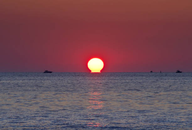 Motorboats on the water near the solar disk against the background of a ruby sky. Sochi, Russia, 2021