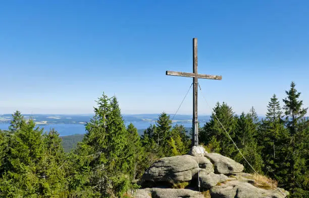The summit cross of the popular excursion destination "Bärenstein" (1077 m). In the background you can see the Vltava reservoir (Lipno).