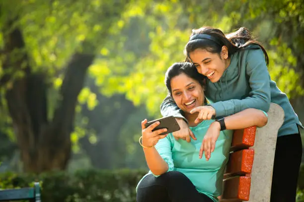 Photo of Mother and daughter laughing while using mobile phone