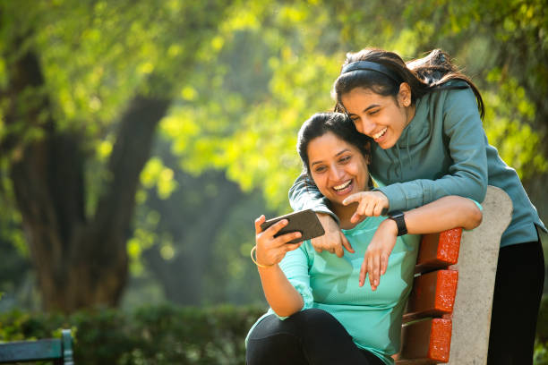 mother and daughter laughing while using mobile phone - using phone garden bench imagens e fotografias de stock