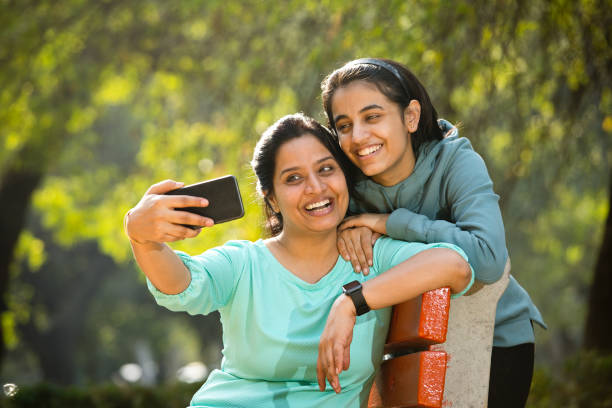 mother taking selfie with daughter at park - using phone garden bench imagens e fotografias de stock