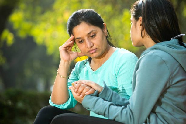 Daughter comforting her mother suffering with headache at park stock photo