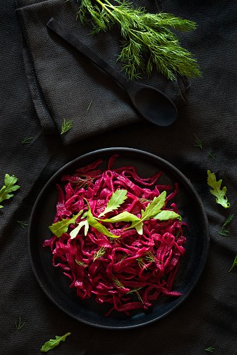 Dark still life photo of a beetroot vegan pasta plate with some arugula and fennel