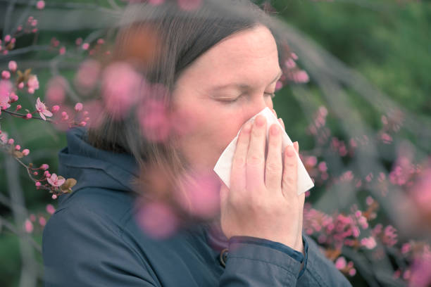 istock Woman sneezing in front of blooming cherry tree in spring 1361258740