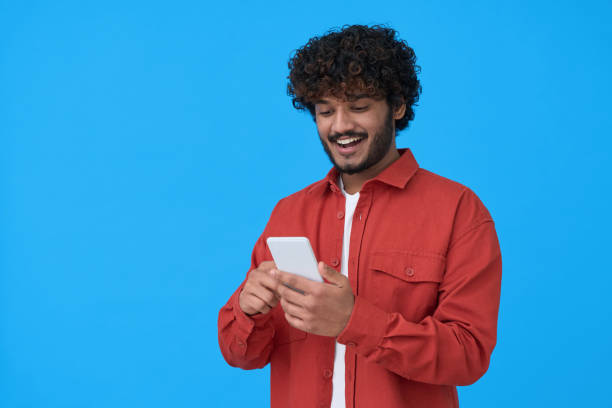 Happy indian young man using mobile phone isolated on blue background.
