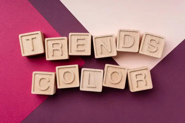 Photo of Color trends 2022, flat, lay, top view. The inscription is made of eco-friendly wooden cubes. Concept trends 2022 against the background of burgundy and Calming coral. Bright geometric background
