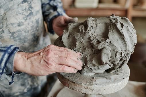 Close-up of male potter working with clay, he making form of sculpture on pottery wheel