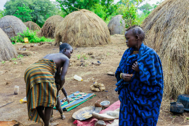 zwei frauen mit ihren kleinkindern in heller kleidung, die im örtlichen mursi-stammesdorf miteinander reden - mursi tribe people ethiopia mother the human body stock-fotos und bilder