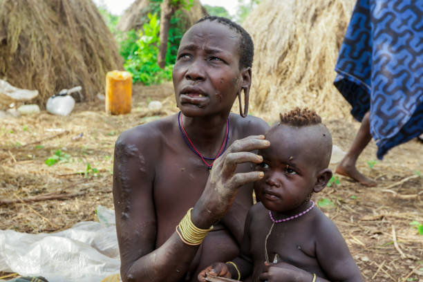 frau mit ihrem säugling mit großen löchern in den ohren posiert vor den touristen im lokalen mursi-stammesdorf - mursi tribe people ethiopia mother the human body stock-fotos und bilder