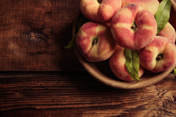 Fresh ripe donut peaches in bowl on wooden table, top view. Space for text