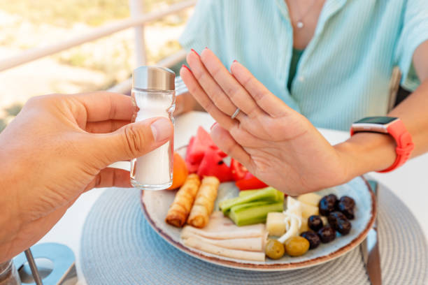 Woman in a restaurant refuses the offered salt and pepper shaker with a gesture of her hand. Diet for gout and high cardiovascular blood pressure stock photo