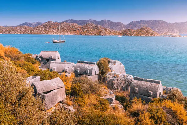 Ancient tombs of the Lycian Greek civilization on the coast of the Mediterranean Sea near the island of Kekova. Travel destinations in Turkey. Cruise yacht sailing in idyllic bay