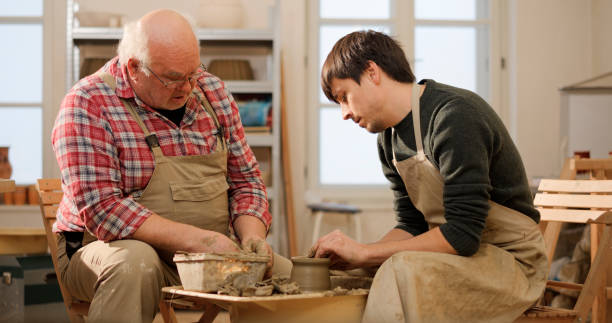 istock Senior male potter teaching a student how to shape a bow on the wheel 1361290655