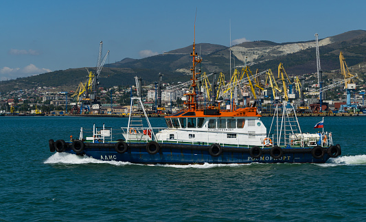 Sea Pilot 'Adis' is sailing in blue water Black Sea. White work boat 'Adis' on Novorossiysk Commercial Sea Port and Caucasus mountains  background.  Novorossiysk, Russia - September 15, 2021