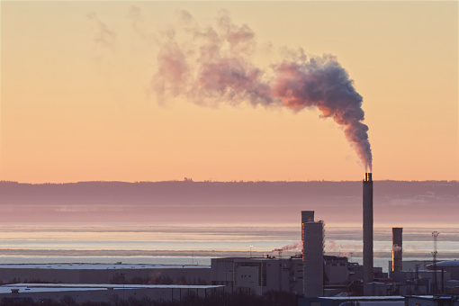 Image presents a single industrial facility that is emitting smoke into the morning sky. Air pollution and greenhouse effect. Background image with plenty of copy space.