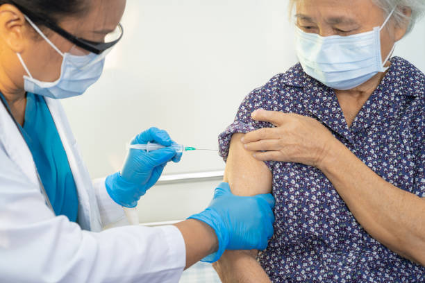 Elderly Asian senior woman wearing face mask getting covid-19 or coronavirus vaccine by doctor make injection. stock photo