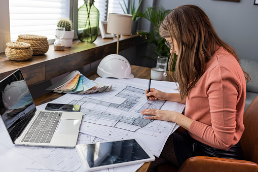 Architecture, building, construction and real estate concept - Happy smiling female architect with blueprint, ruler and living house model on table working at home office. Architect woman.