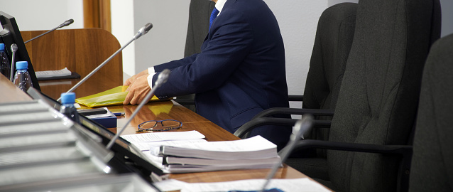 A man sits in an armchair at a table with monitors and speakerphones and goes through documents. Conference hall. Politician, lawyer or businessman. Without a face