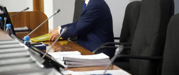 Photo of A man sits in an armchair at a table with monitors and speakerphones and goes through documents. Conference hall. Politician, lawyer or businessman