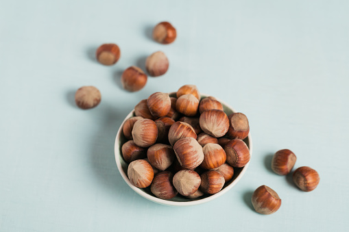 Pile of hazelnuts filbert in a bowl on a light blue background. Fresh nuts in their shells.