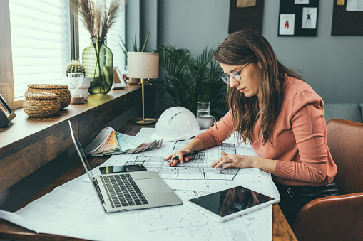 Shot of a young businesswoman working with blueprints in an office. Shot of an attractive young architect working in her office. Female architect working at home. She looking at blueprint