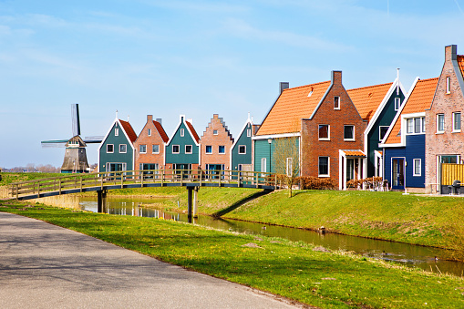 Panorama with modern brick houses along water in a family friendly suburban neighborhood in Volendam in the Netherlands. Typical Dutch houses and windmill on background