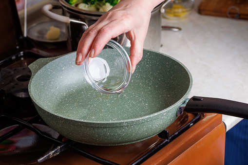senior caucasian woman hand pouring vegetable oil on empty preheated skillet.